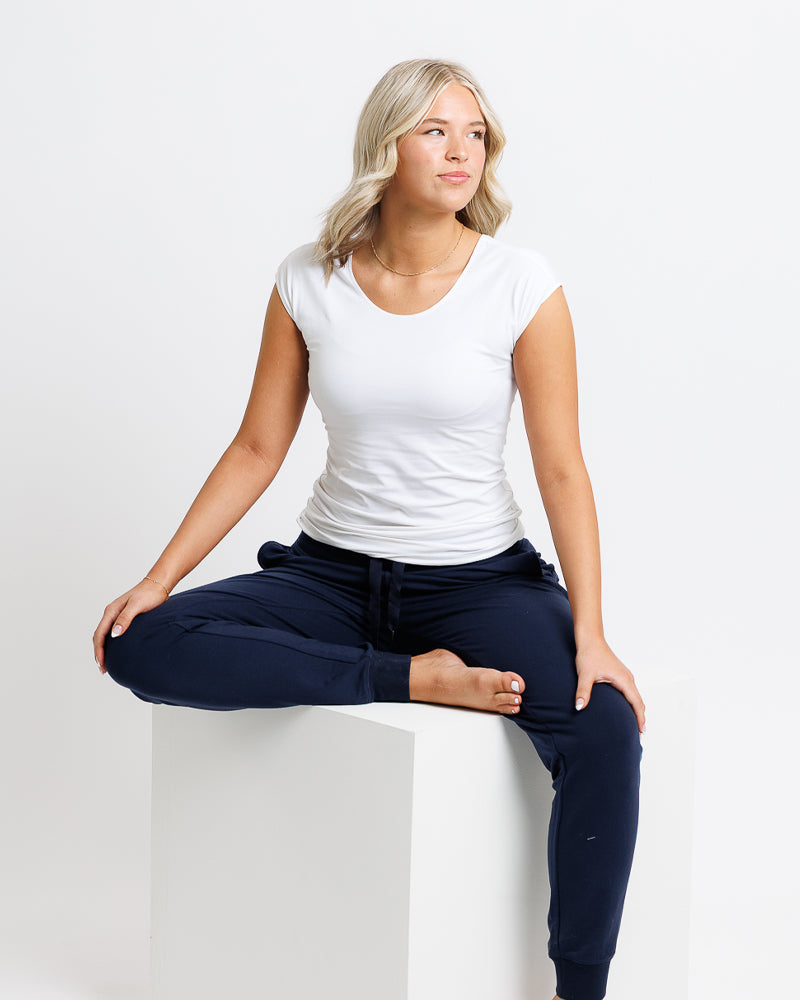 Woman sitting on a white stool wearing a white t-shirt and navy blue pants