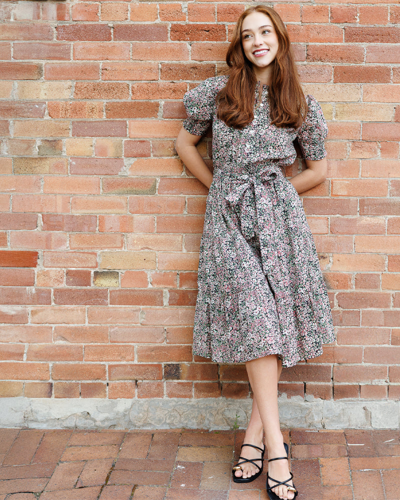 Woman in a floral dress standing against a brick wall