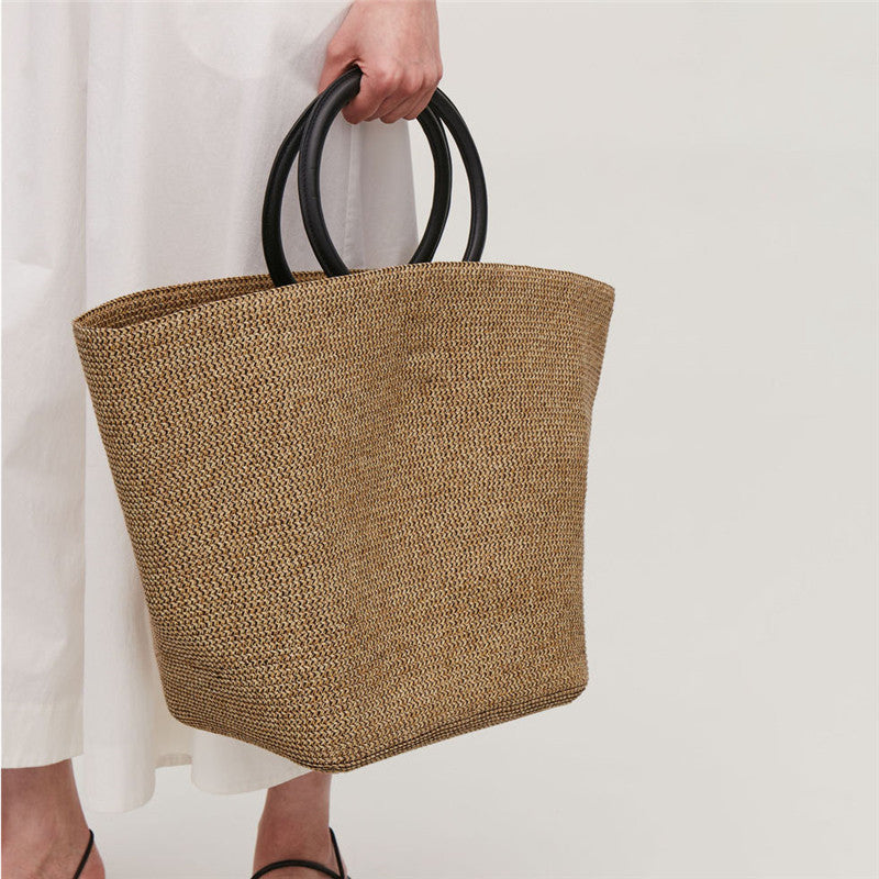 Person holding a woven brown bag with black handles