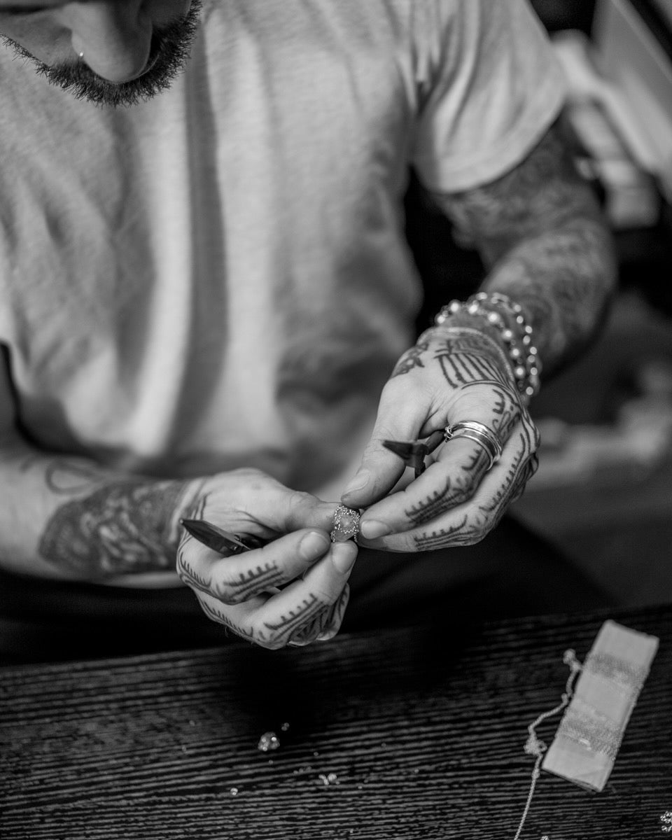 Person with tattoos holding a small object on a wooden surface