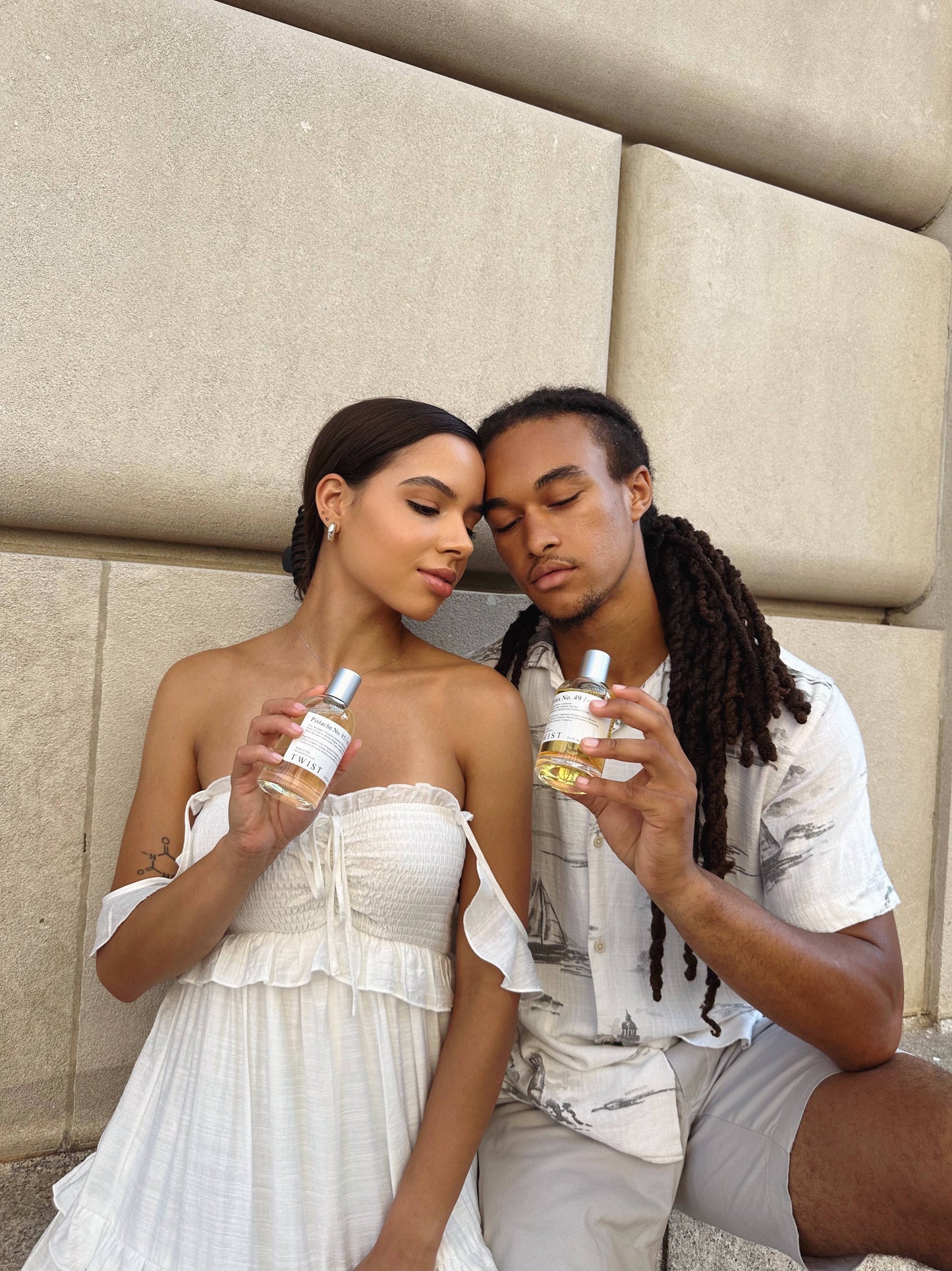 Two people sitting together holding bottles of twist perfume