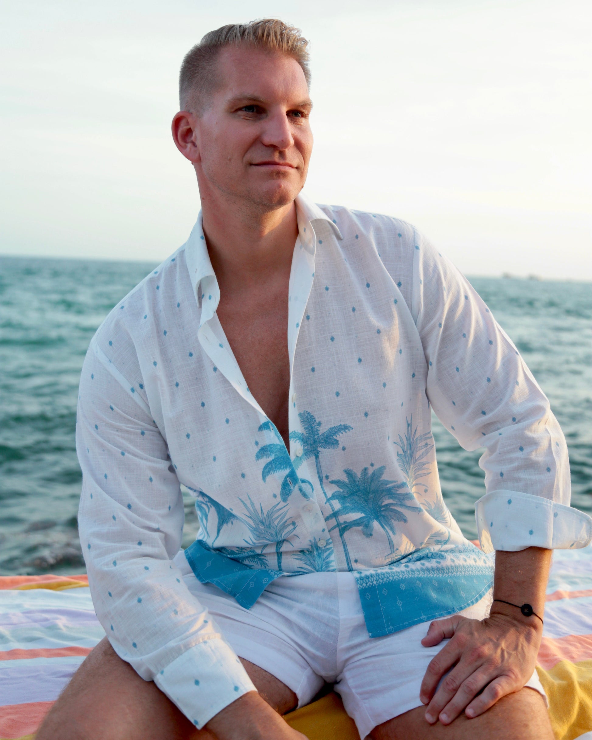 Man wearing a white shirt with blue palm tree design by the ocean