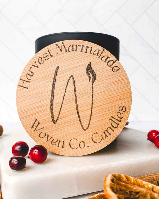 Candle with wooden lid featuring 'Harvest Marmalade Woven Co. Candles' branding. Candle with wooden lid featuring 'Harvest Marmalade Woven Co. Candles' branding.