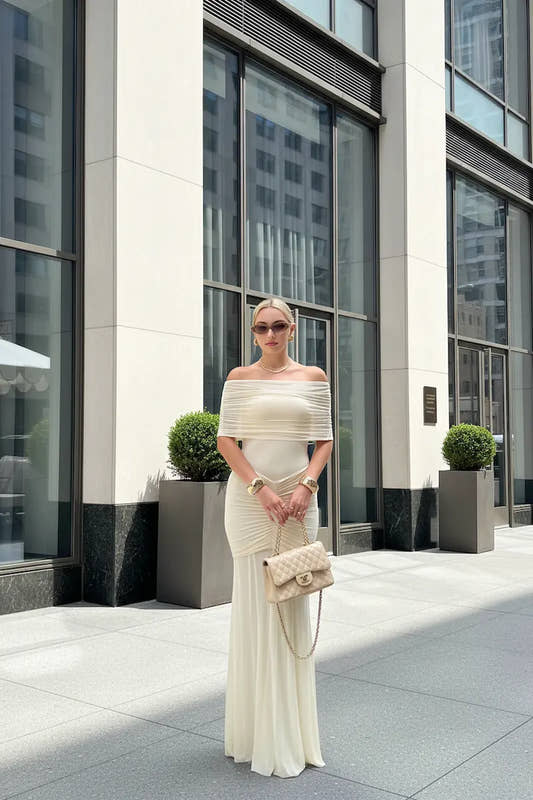 Woman in a white off-shoulder dress standing in front of a modern building. Woman in a white off-shoulder dress standing in front of a modern building.
