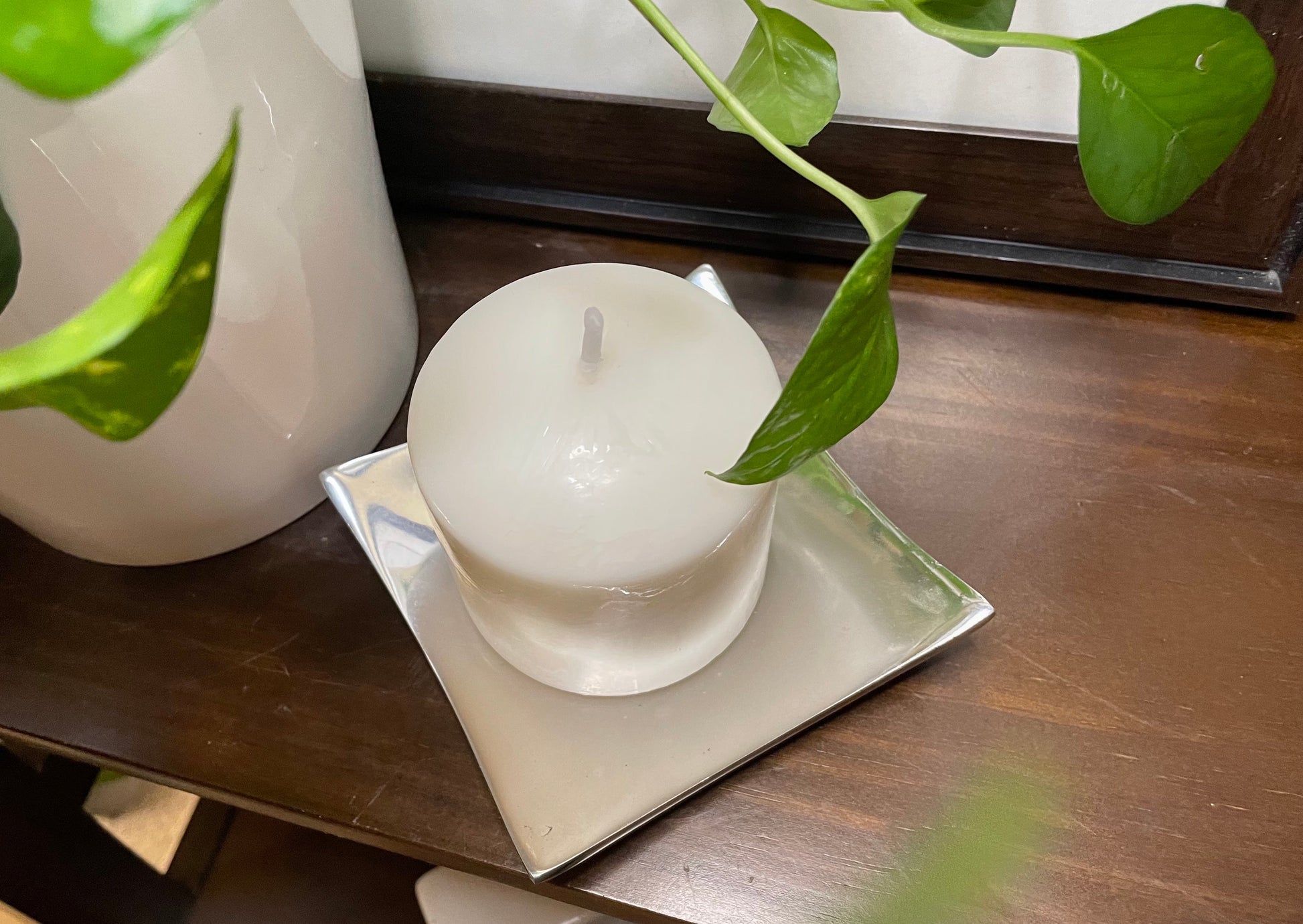White candle on a square plate with green leaves on a wooden surface