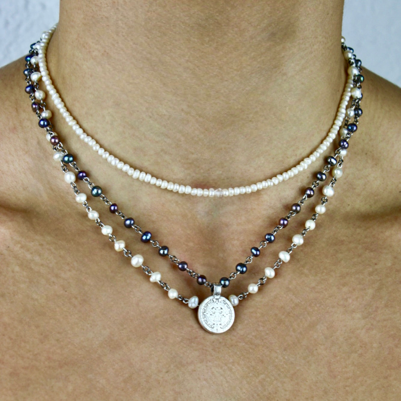 Two pearl necklaces with a silver pendant on a person's neck against a neutral background
