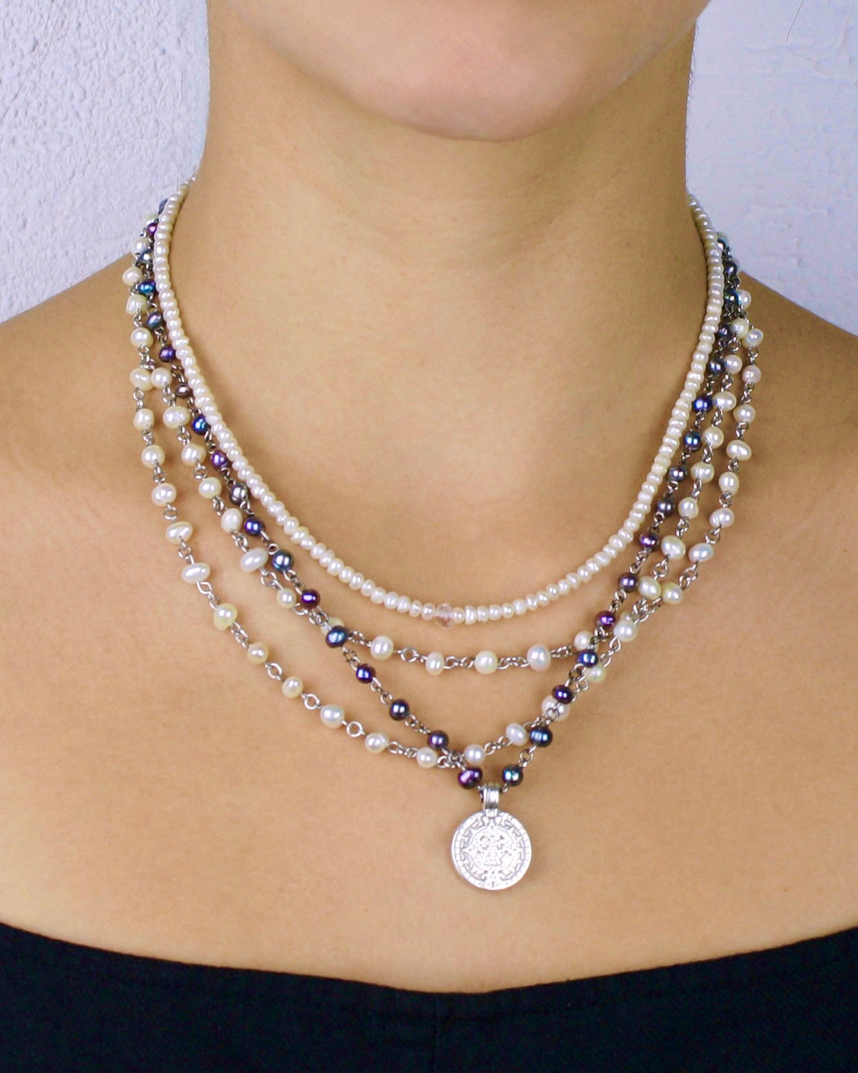 Layered pearl and beaded necklace with a silver pendant on a person against a neutral background