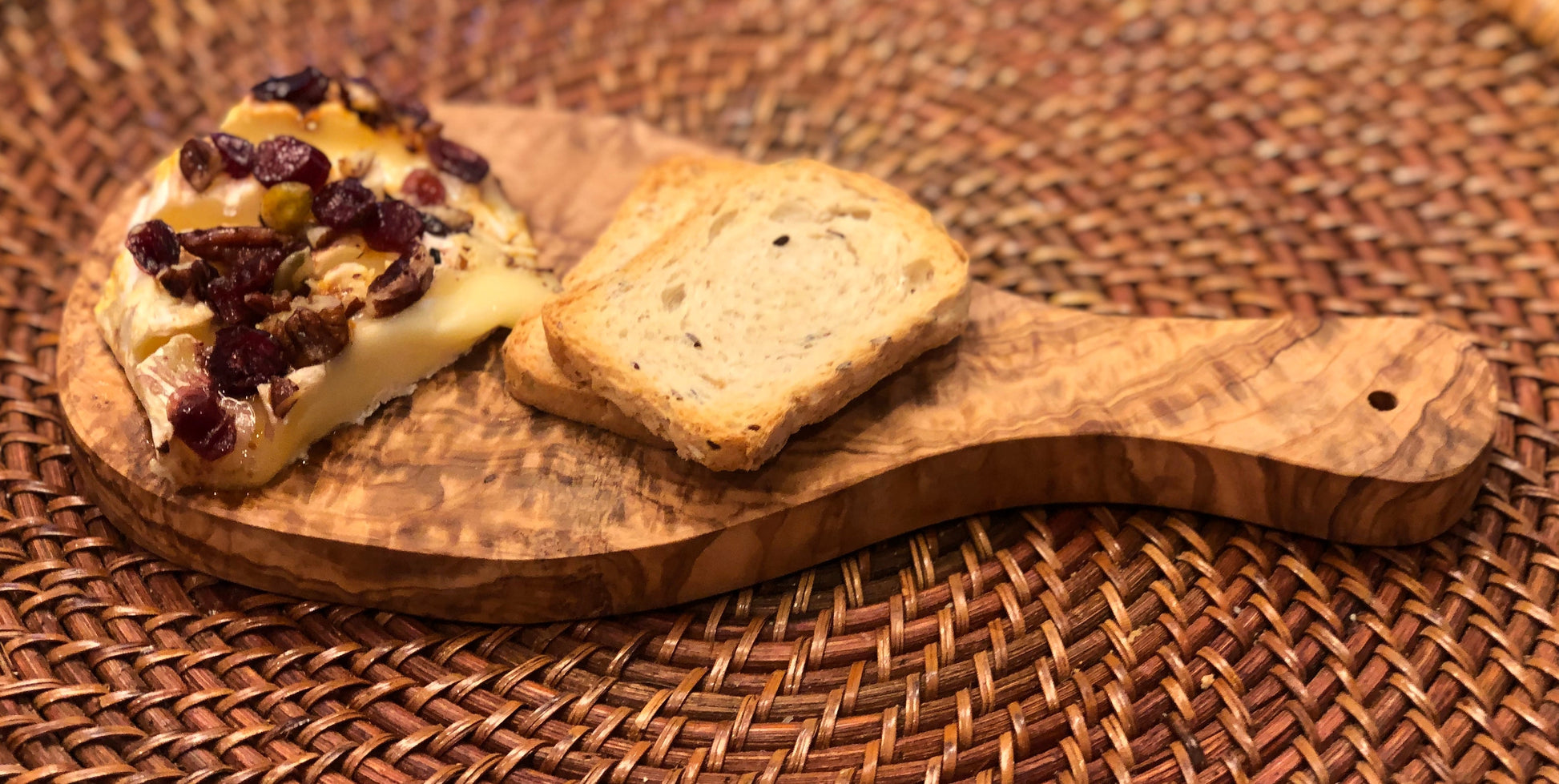 Wooden board with cheese and cranberries on a woven surface