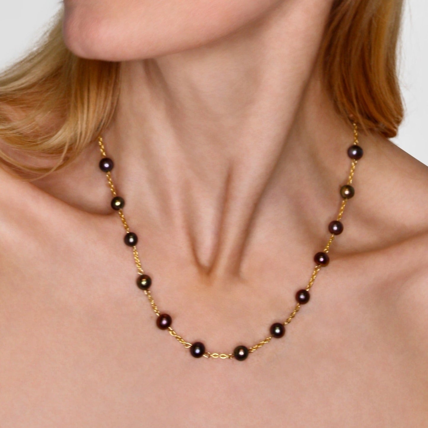 Gold necklace with black beads worn by a person on a plain background