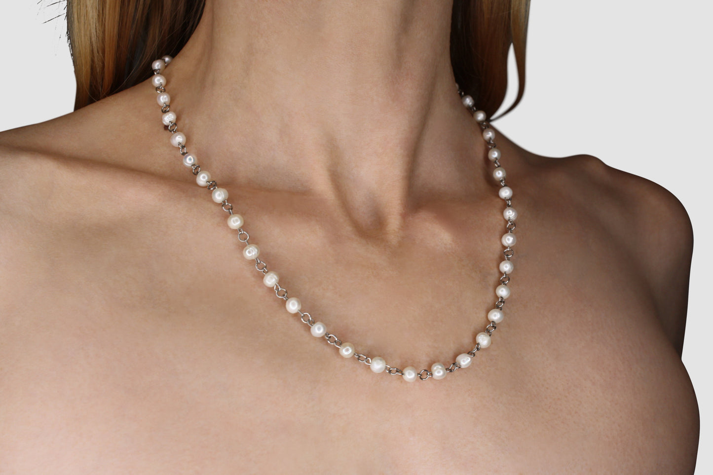 Pearl necklace being worn by a person on a plain background
