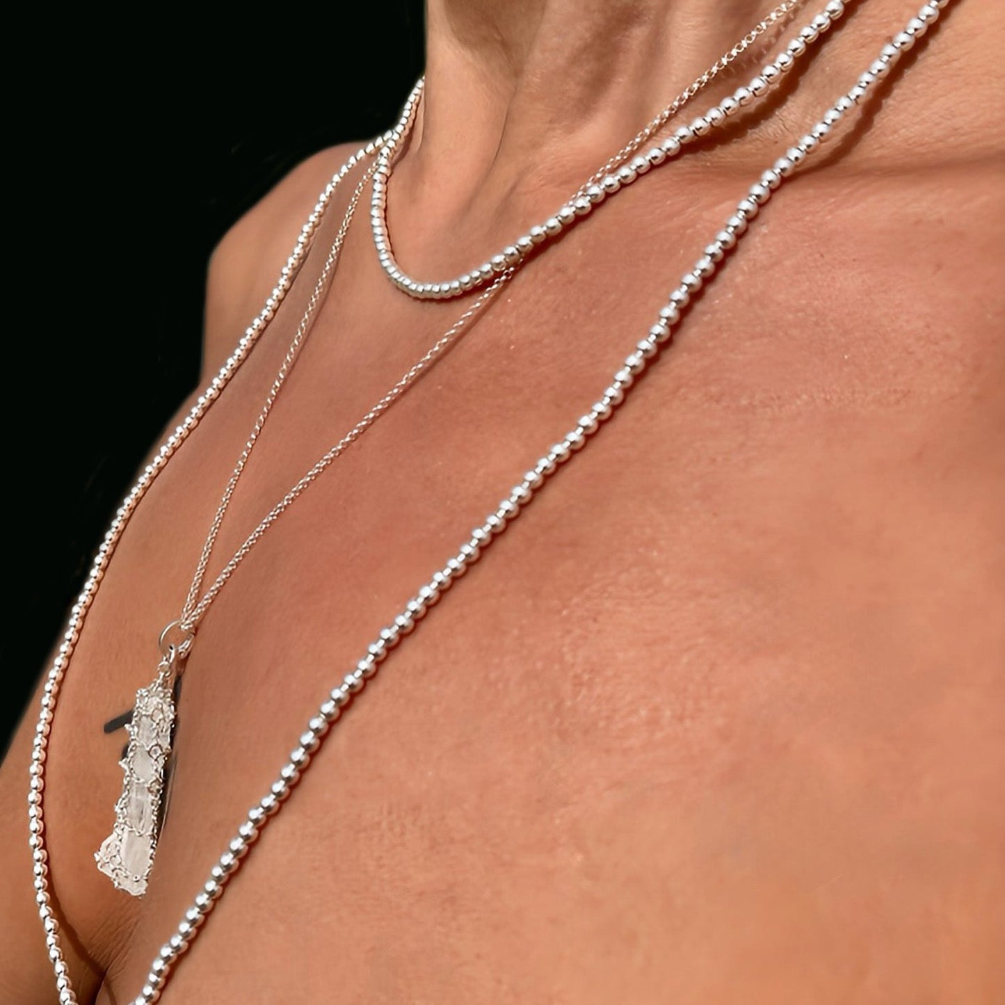 Close-up of a person wearing multiple silver necklaces with a dark background