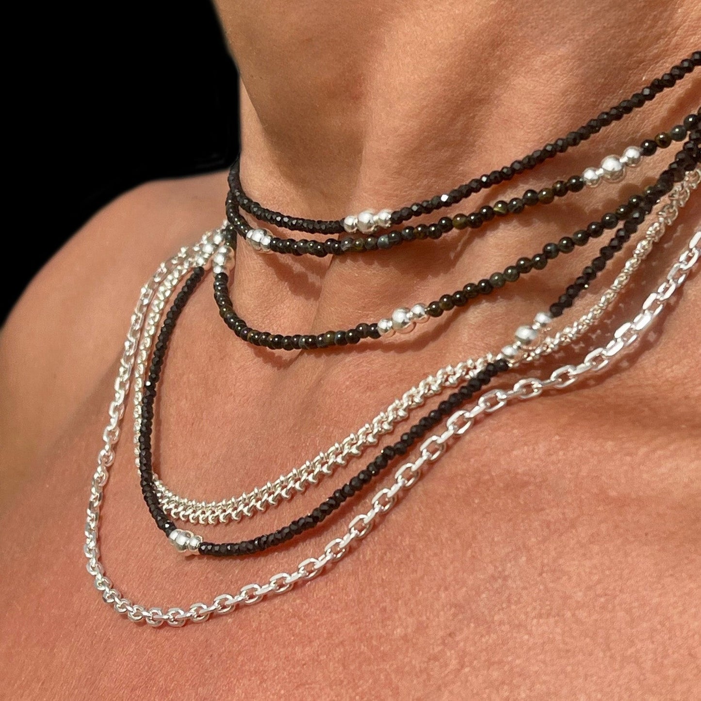 Necklace with black and silver beads and chains on a person's neck against a dark background