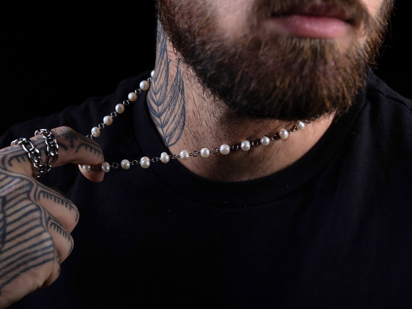 Man with tattoos holding a pearl necklace against a black background