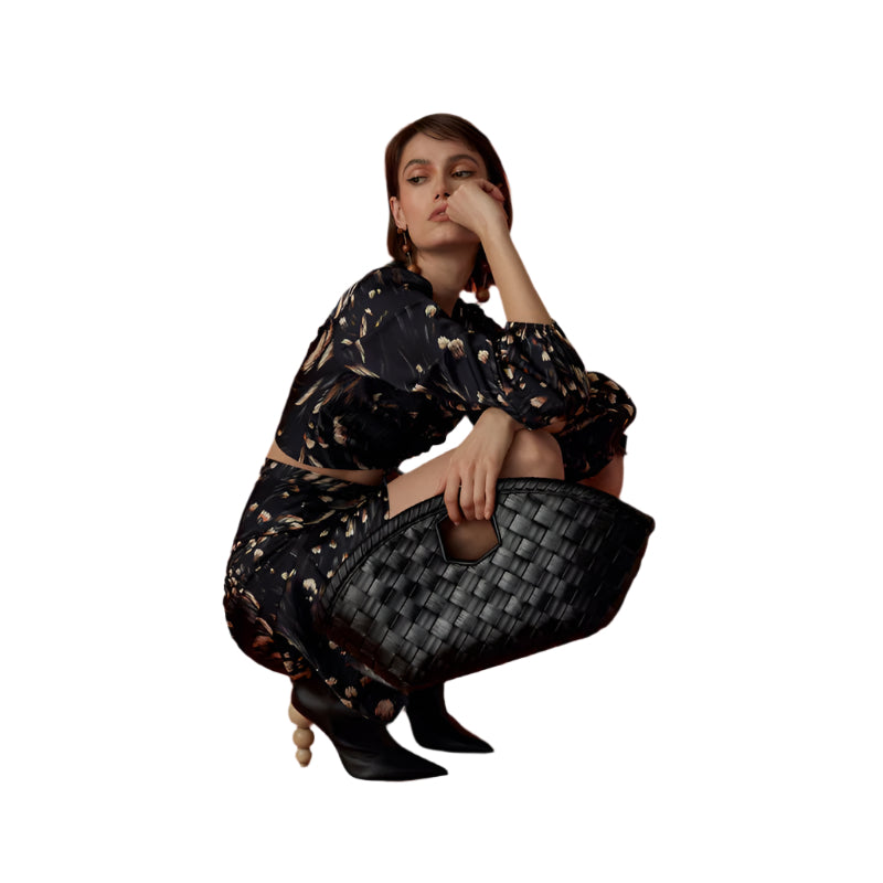 Woman in a black patterned outfit holding a textured bag  made of leather