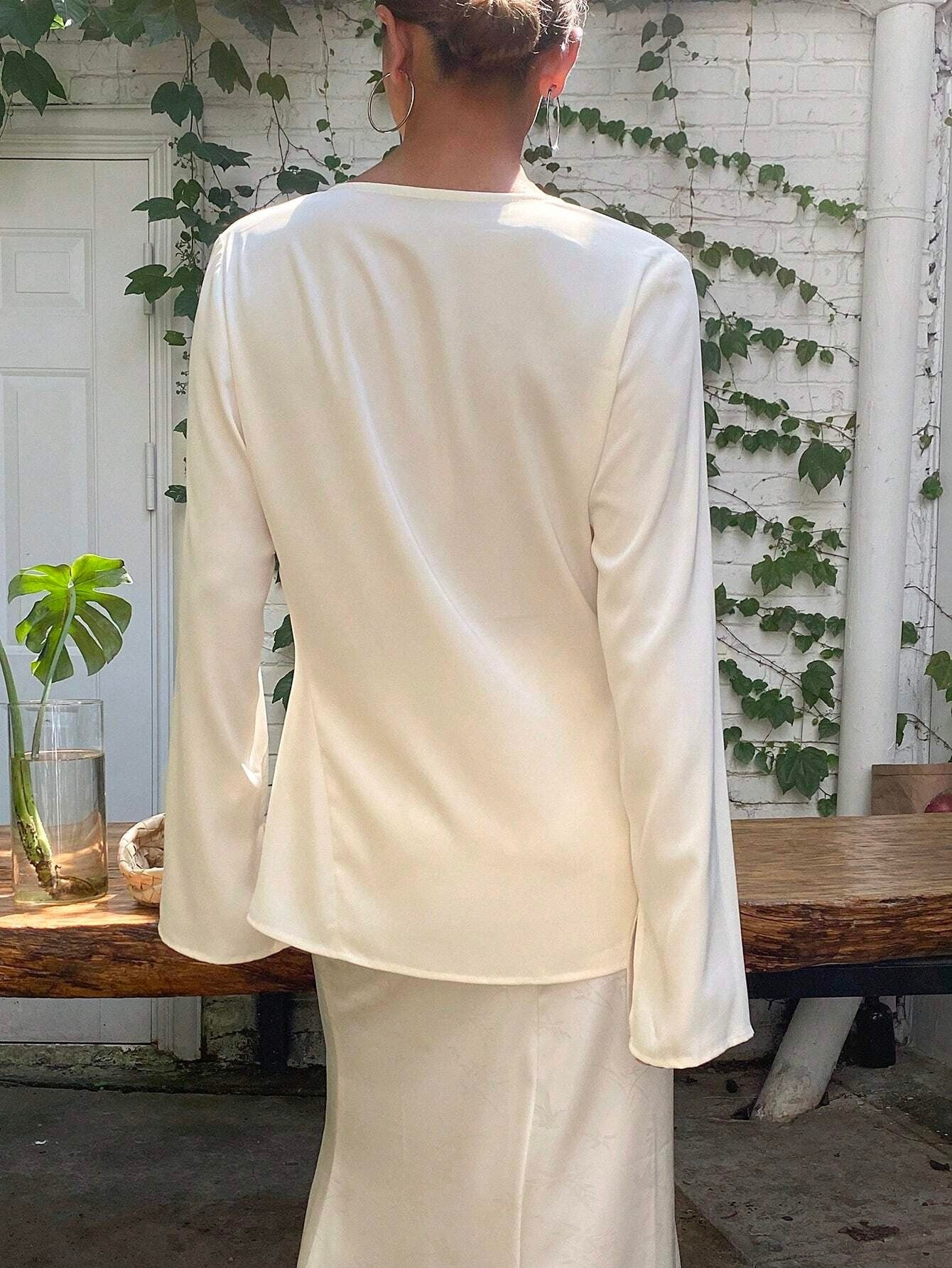 Person wearing a white outfit standing in front of a white wall with greenery