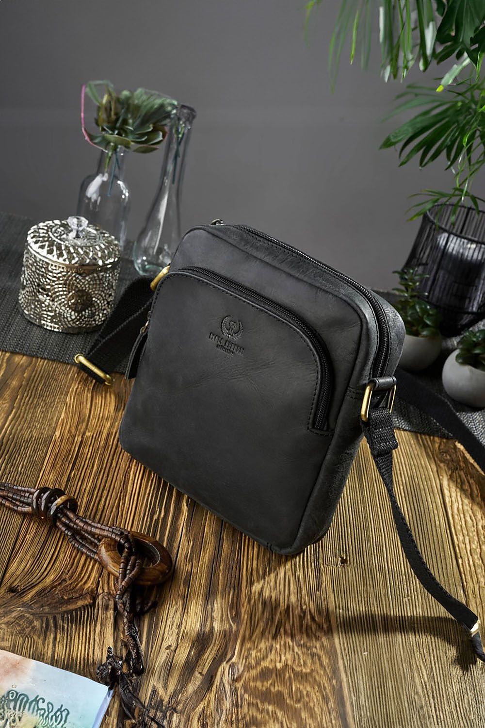 crossbody black leather bag on a wood table