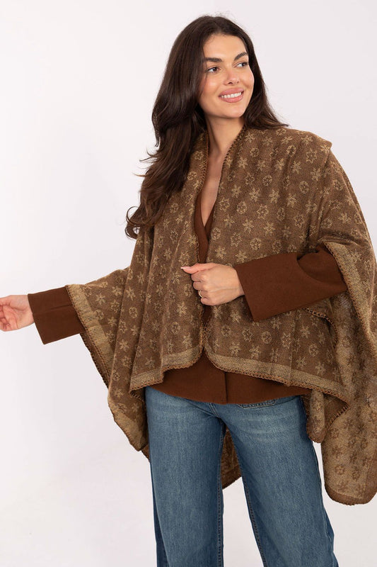 Woman wearing a brown patterned poncho over a brown top and blue jeans  Woman wearing a brown patterned poncho over a brown top and blue jeans