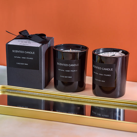Two black scented candles with labels on a reflective surface  Two black scented candles with labels on a reflective surface