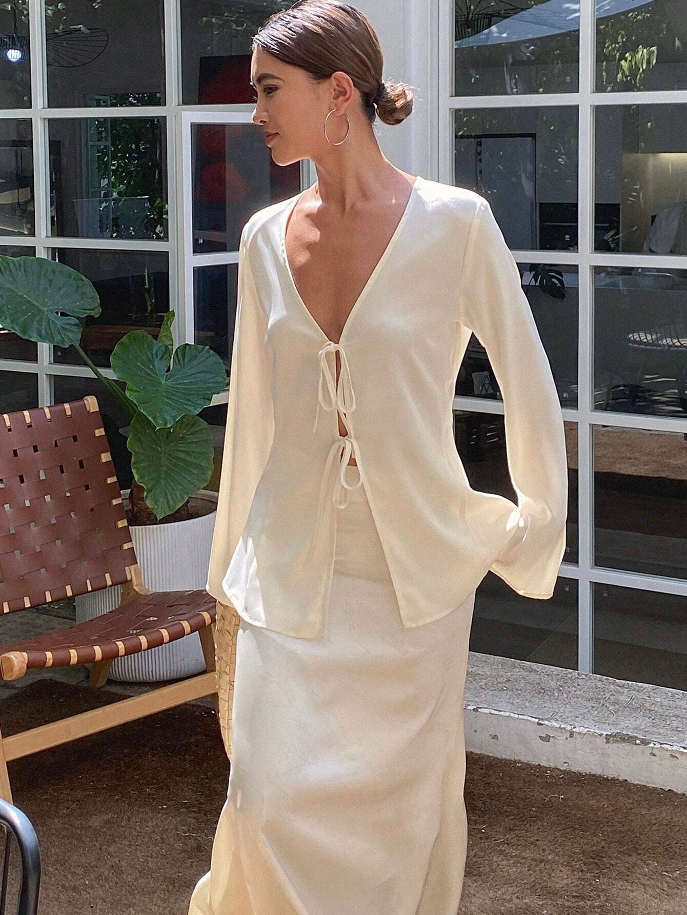 Woman wearing a cream-colored outfit standing in front of a window.