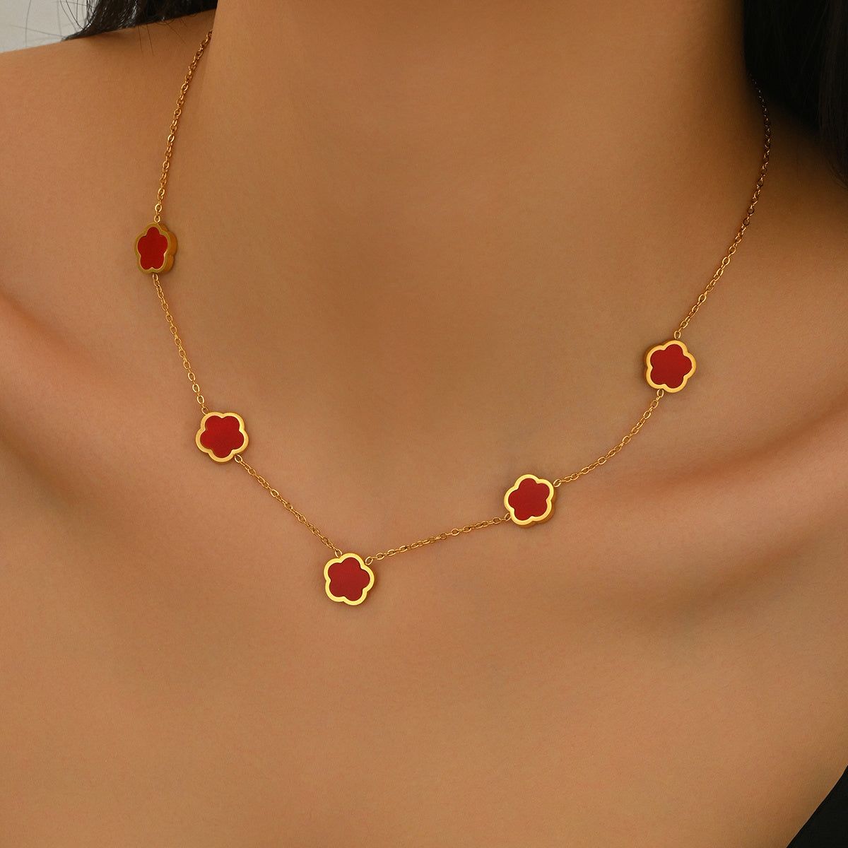 Gold necklace with red flower-shaped pendants on a person's neck