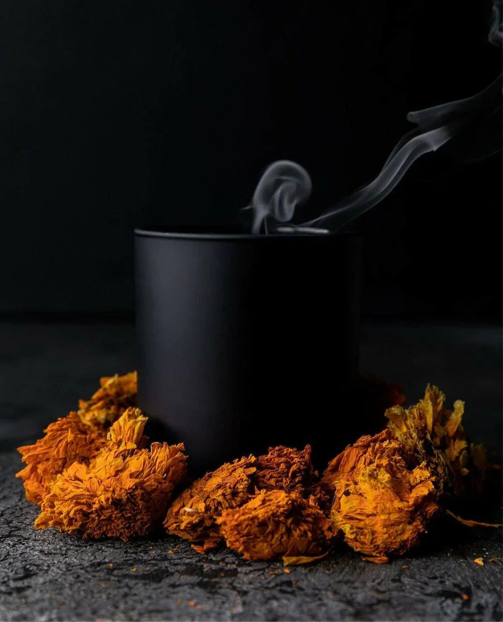 Black mug with steam, surrounded by dried orange flowers