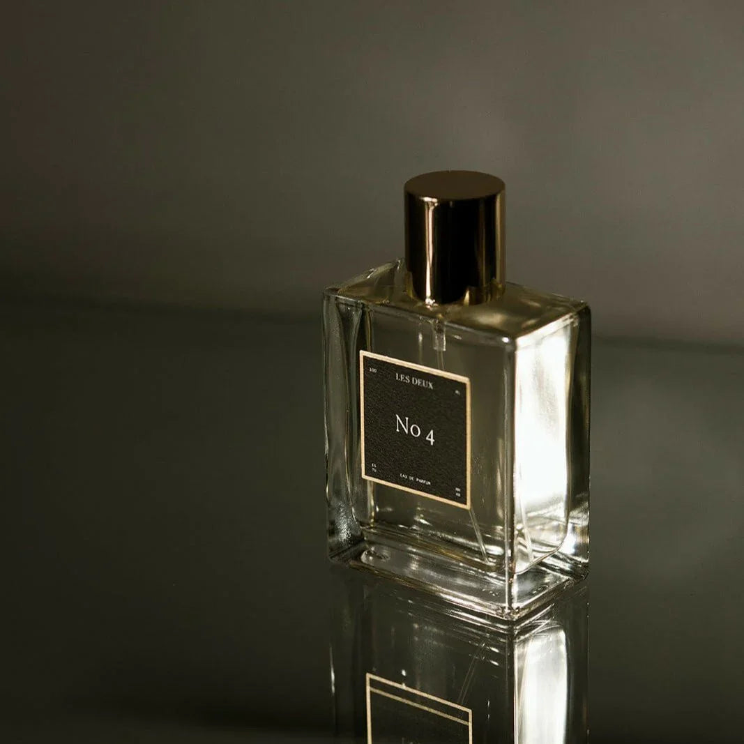 Perfume bottle labeled 'No 4' with a gold cap on a reflective surface.