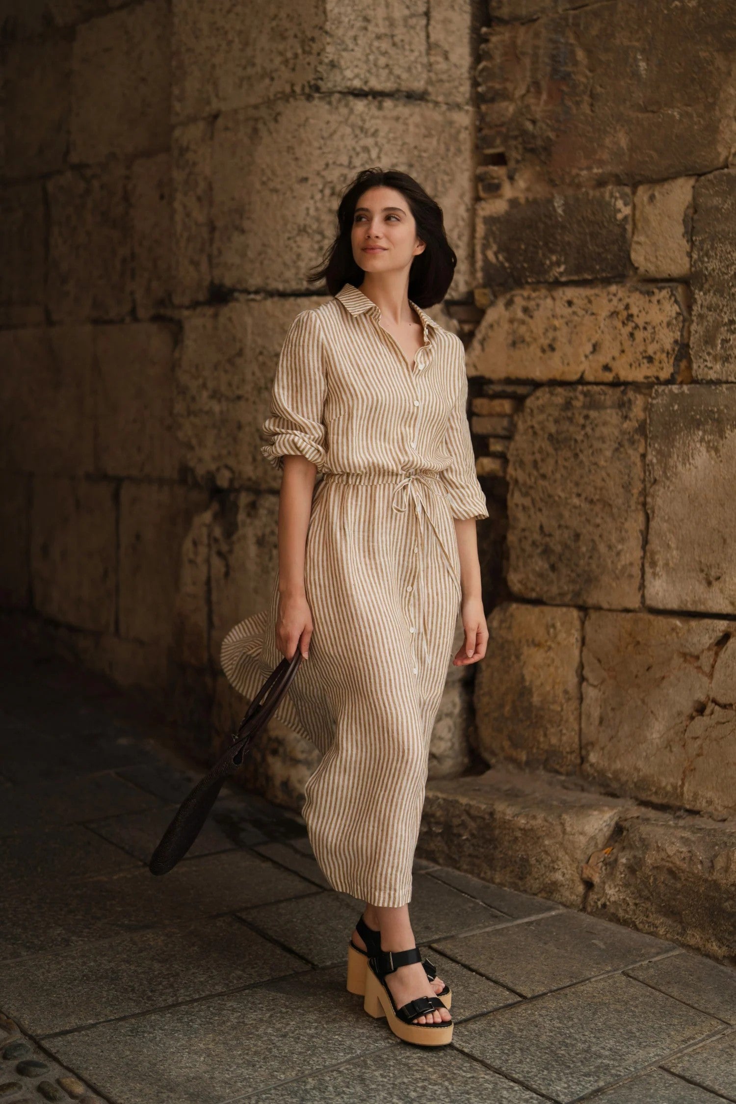 Woman wearing long linen shirt dress with side slits and belt.