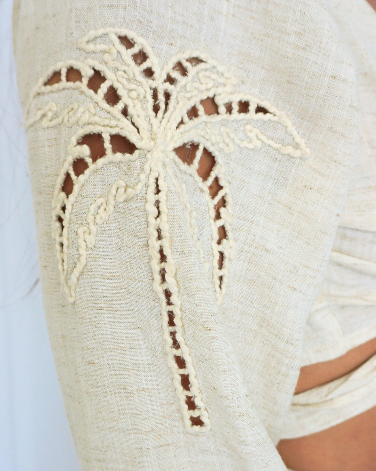 Close-up of a white lace palm tree design on a garment against a white background