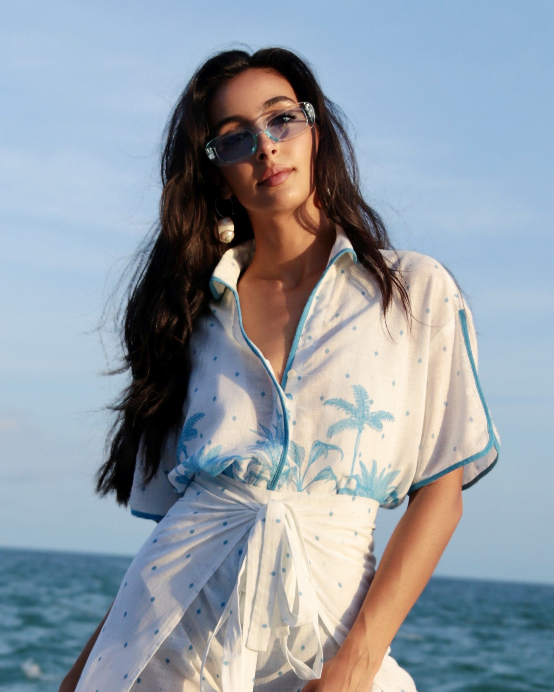 Woman wearing a white and blue outfit with palm tree design against a clear sky.