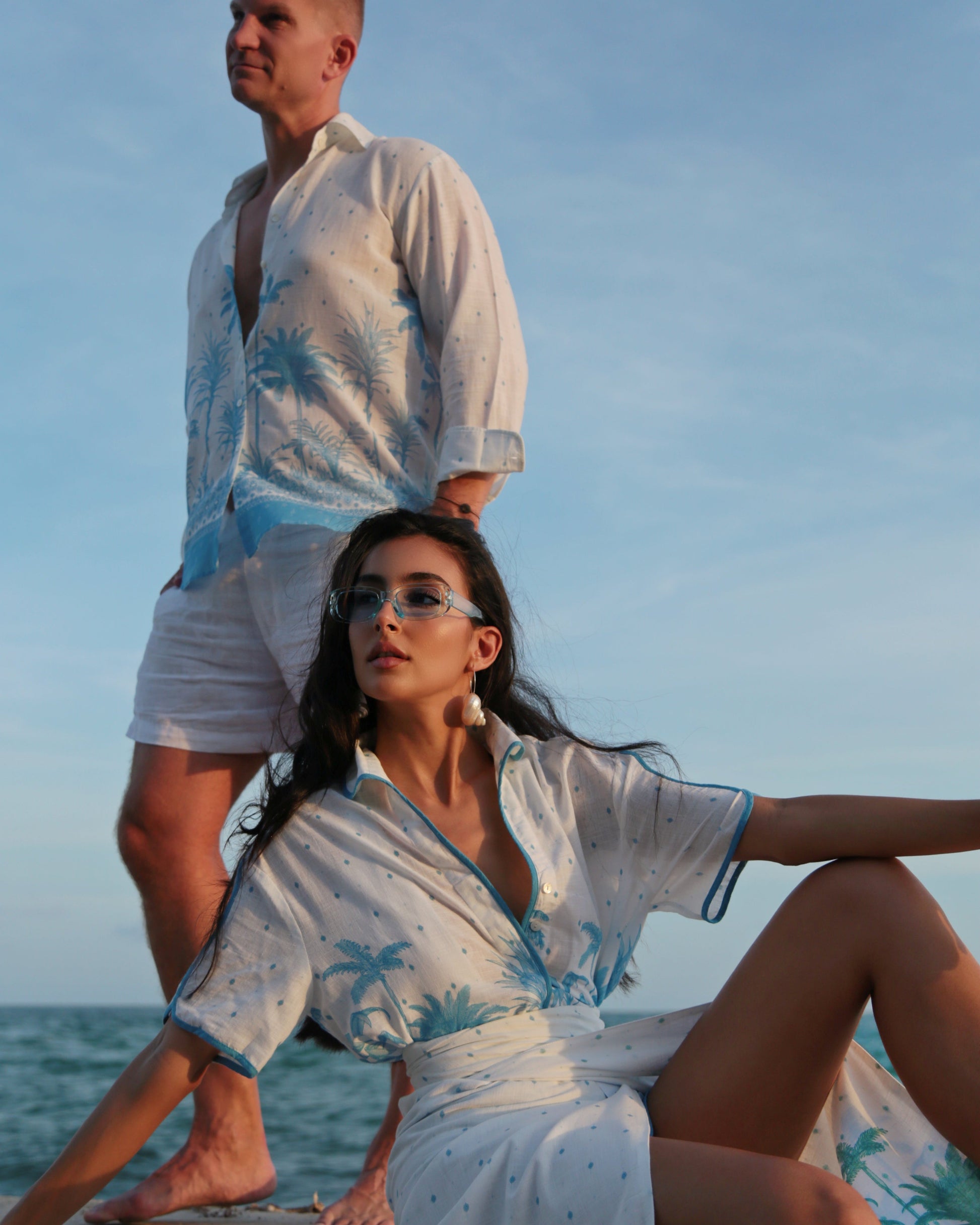 Two people in matching white and blue outfits with palm tree patterns on a boat.