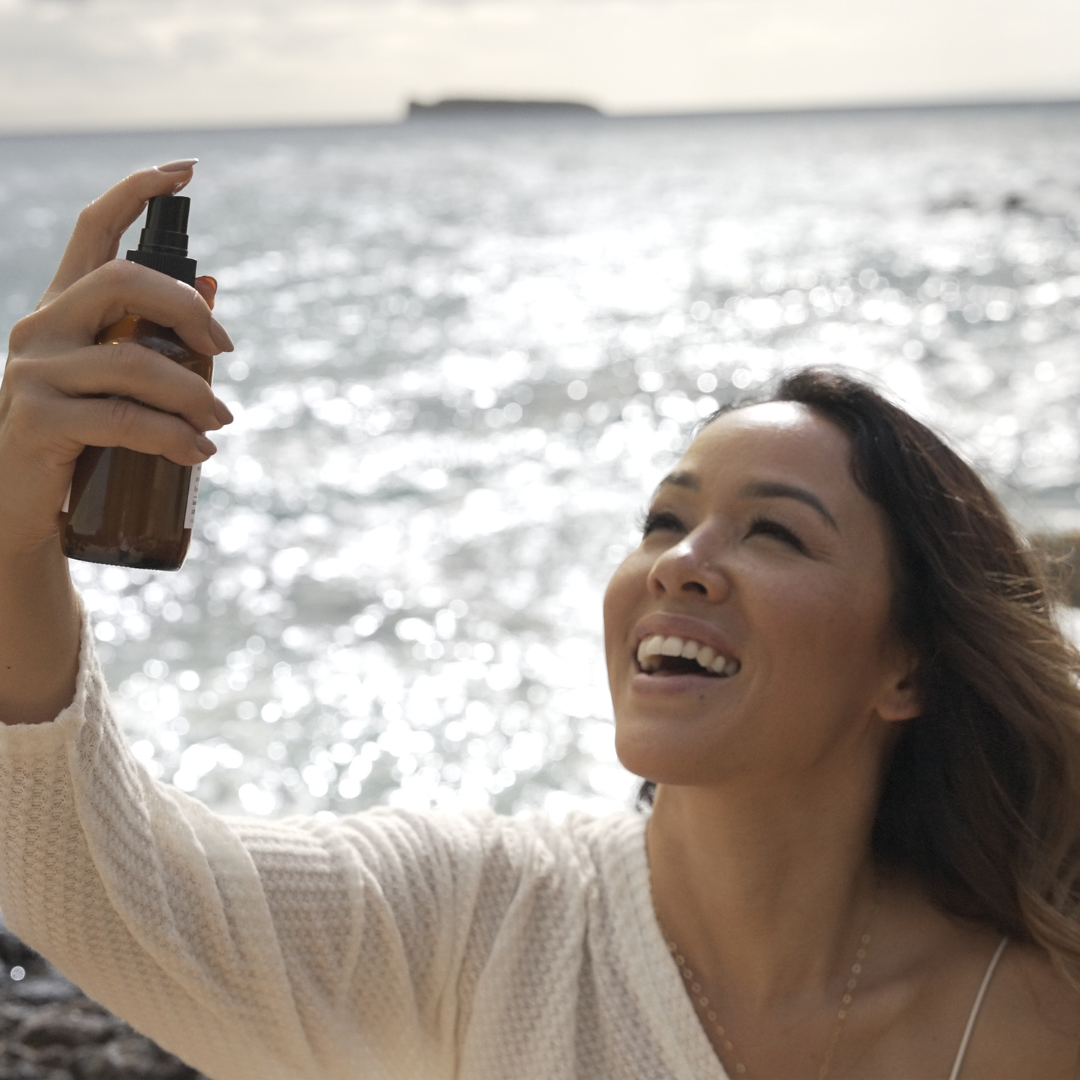 Woman applying sunscreen spray by the ocean