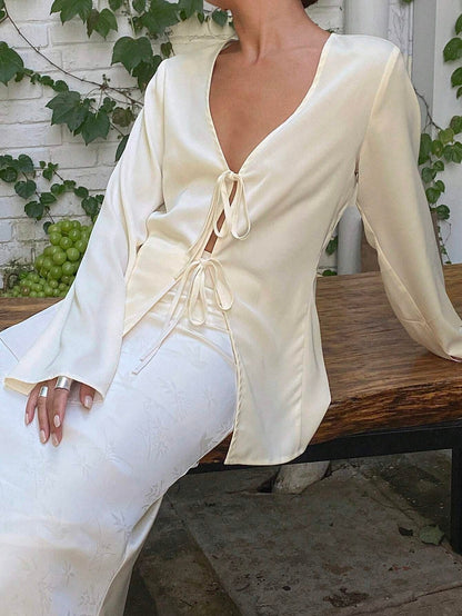 Person wearing a white outfit with long sleeves and lace-up design, sitting on a wooden bench.