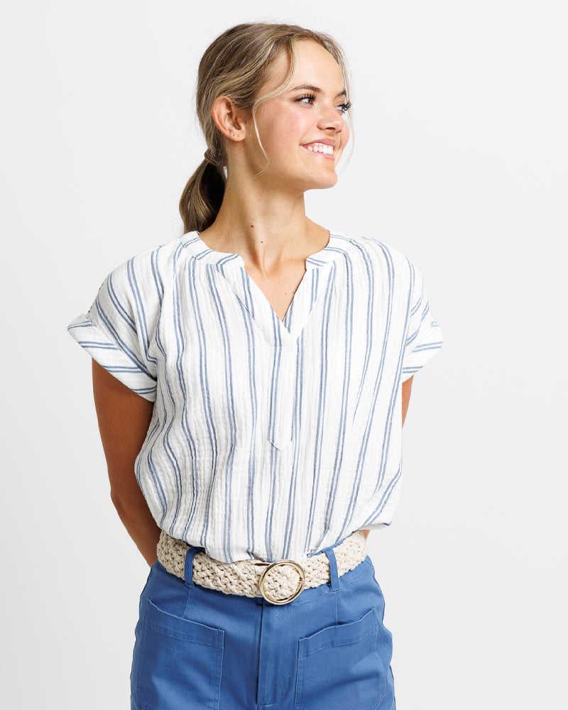 A smiling woman wearing a white Vneck shirt with a skirt and a white belt 