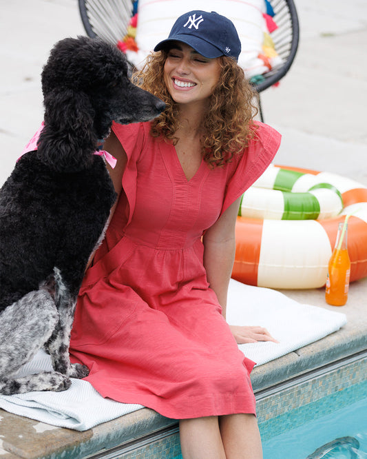 Woman in a beautiful red short dress and blue cap sitting by a pool 