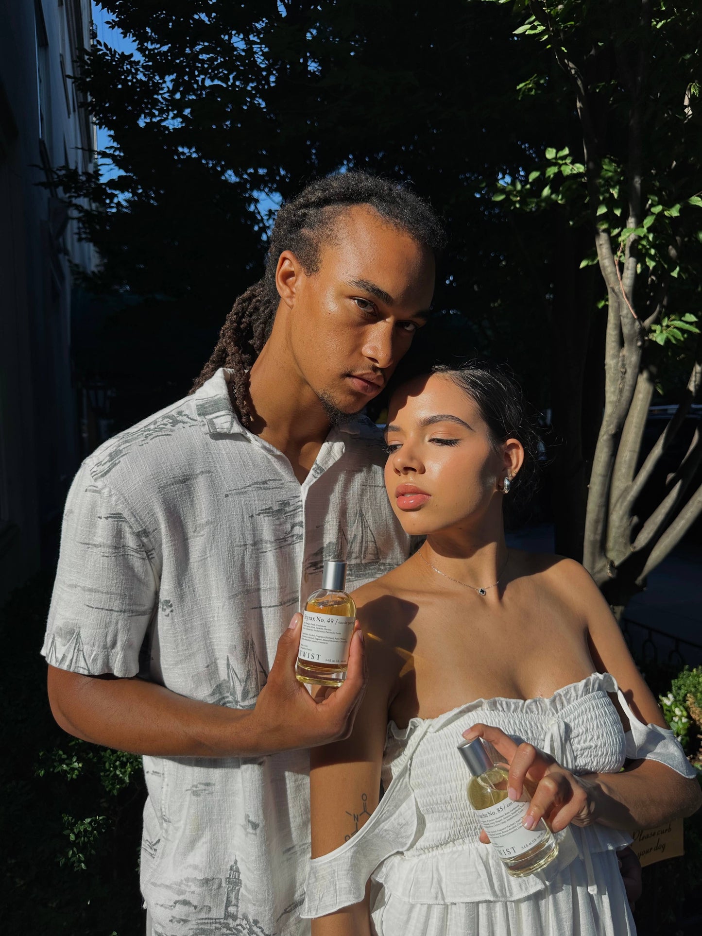 Two people outdoors, one holding a bottle of a twist perfume 