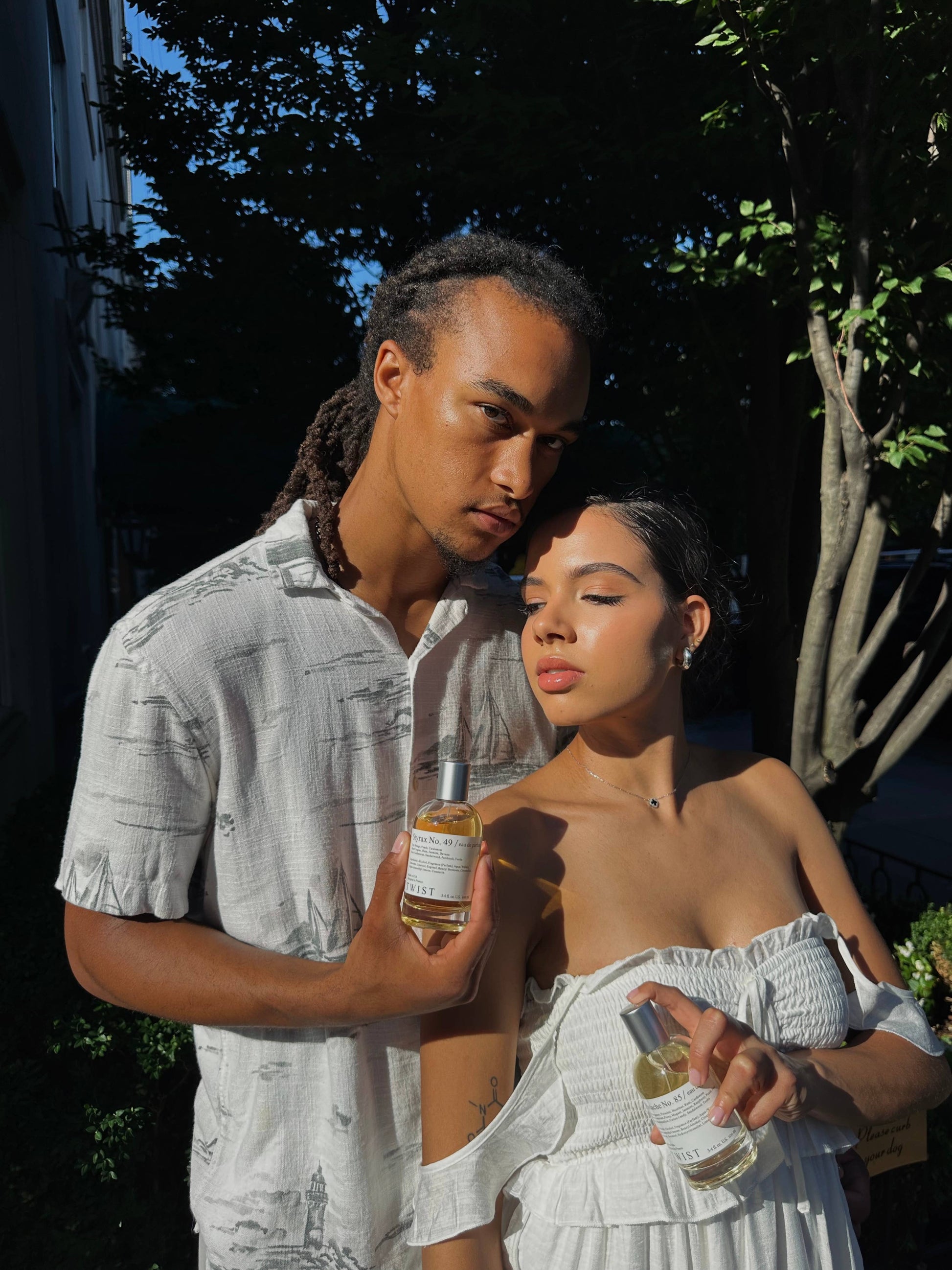 Two people outdoors, one holding a bottle of a twist perfume 