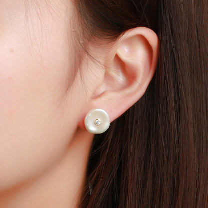 Pearl earring with a diamond on an ear against a neutral background