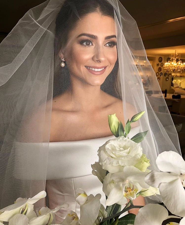 Woman in a wedding dress with a veil and bouquet of flowers indoors.