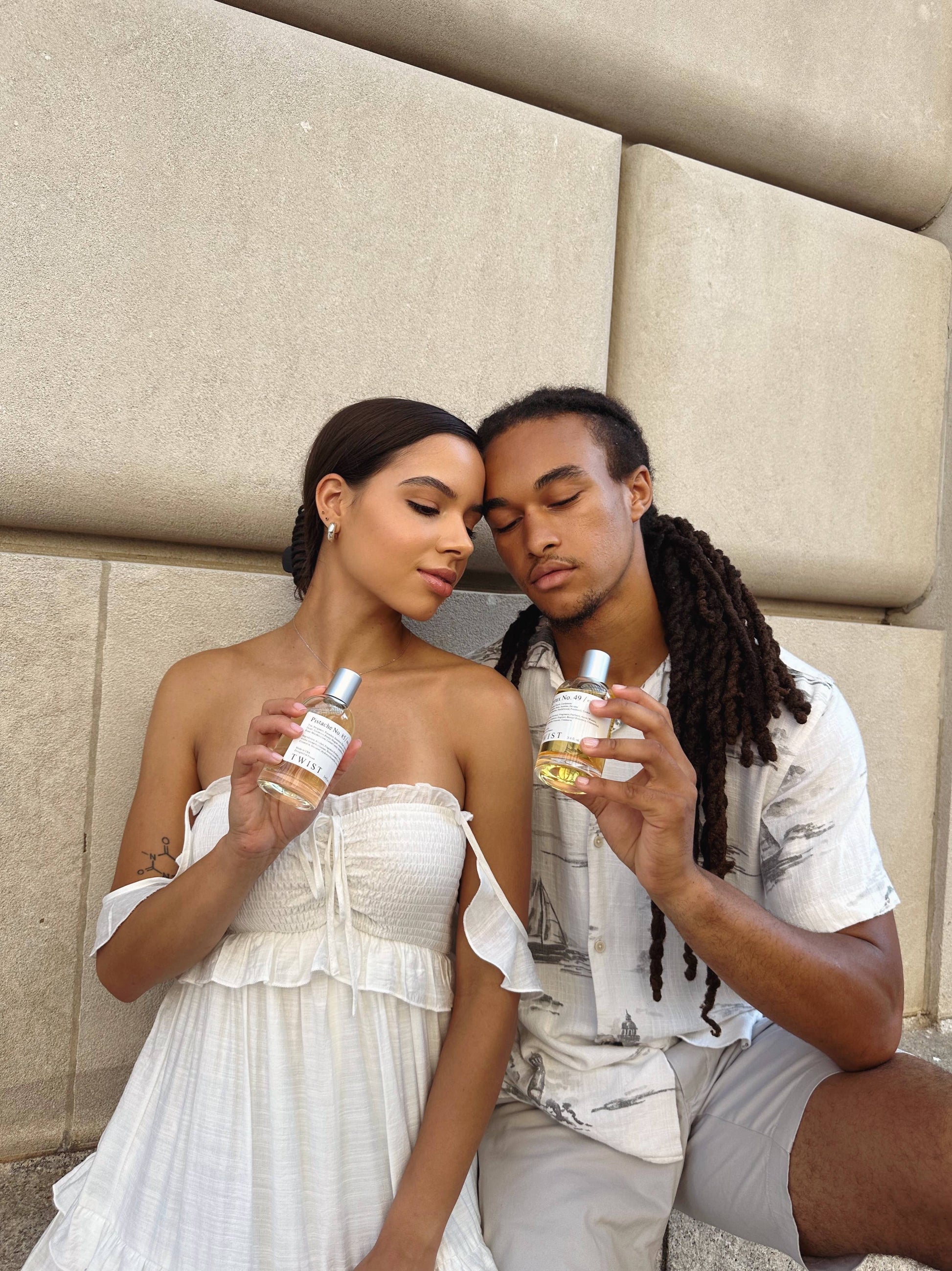 Two people sitting together holding bottles of twist perfume