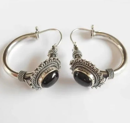 Pair of silver hoop earrings with black stones on a white background