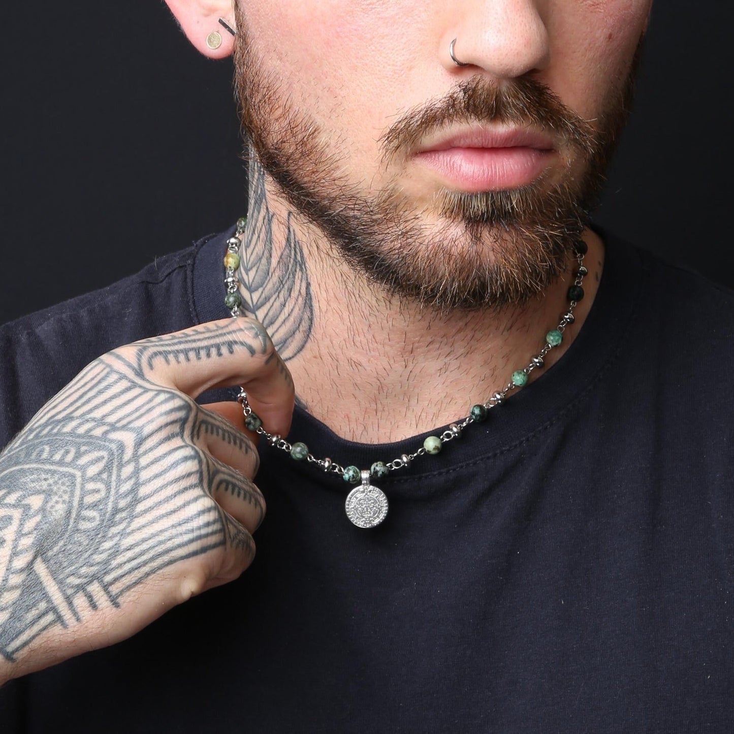 Man with tattoos wearing a necklace against a black background