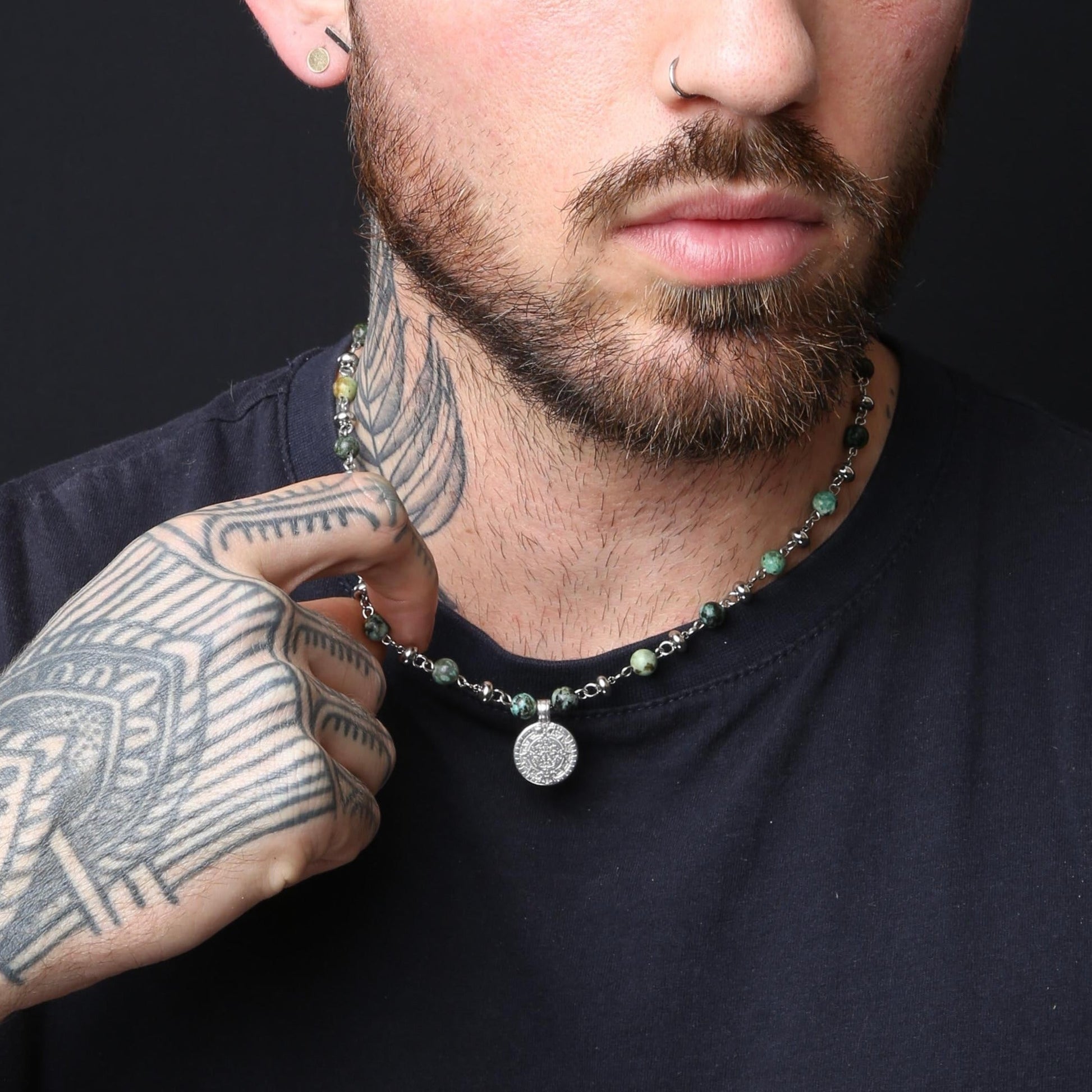 Man with tattoos wearing a necklace against a black background
