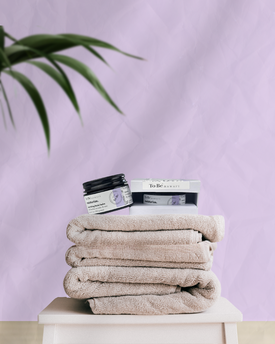 Stack of beige towels with a jar and box of Nourishing Facial Balm - Organic Waterless Moisturizer