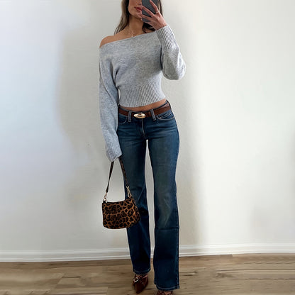 Person wearing a gray off-shoulder cotton sweater and blue jeans, holding a leopard print handbag 