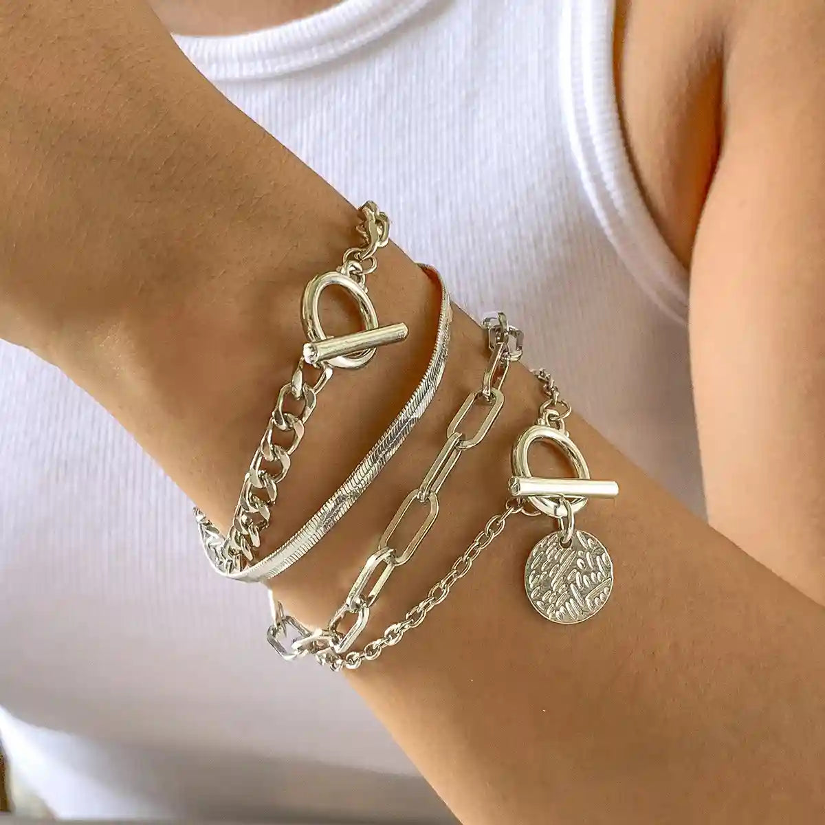 Silver chain bracelets on a wrist with a plain background