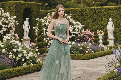 Sage green butterfly tulle gown with spaghetti straps and layered skirt in garden setting 

