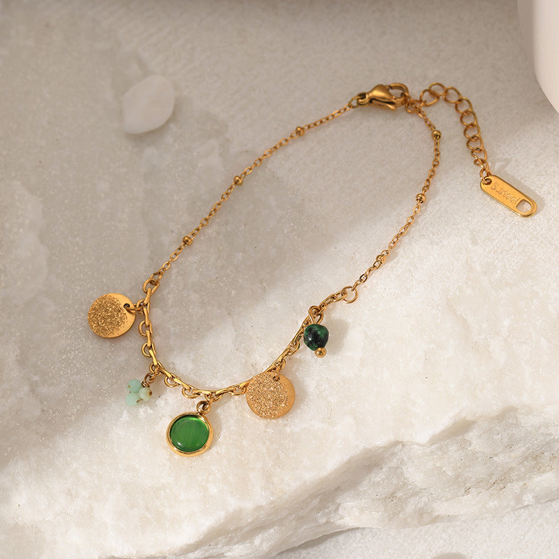 Gold bracelet with green stones on a marble surface