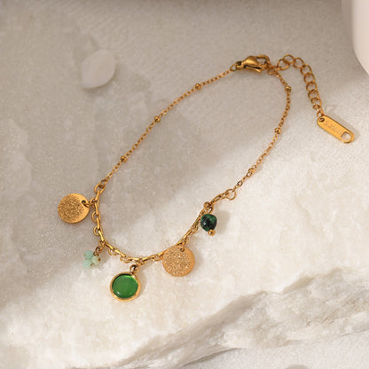 Gold bracelet with green stones on a marble surface