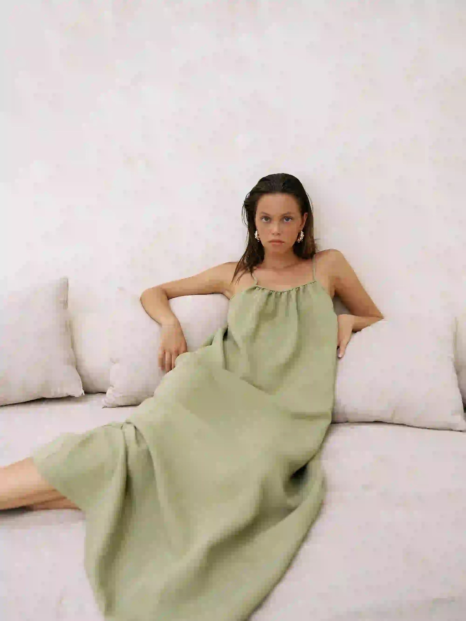 Woman in a green dress lying on a white couch against a white wall