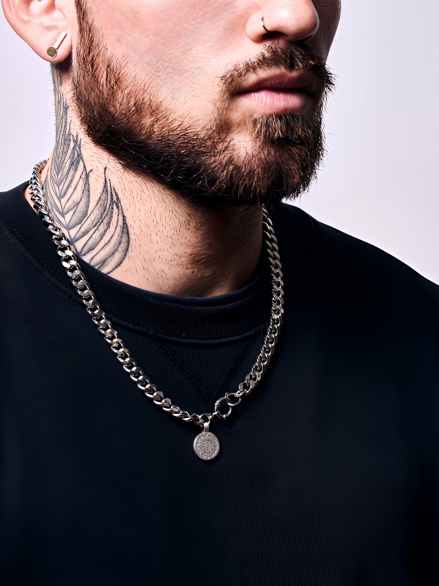 Man wearing a black shirt with a silver chain necklace against a neutral background